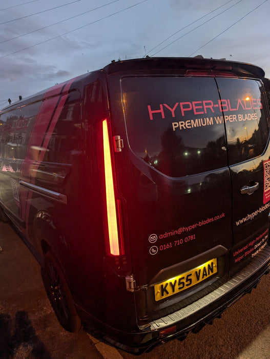 Smoked LED rear light unit illuminated on a black Ford Transit Custom at dusk