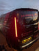 Smoked LED rear light unit illuminated on a black Ford Transit Custom at dusk