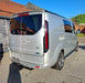 Rear three-quarter view of a silver Ford Transit Custom with smoked LED rear light units